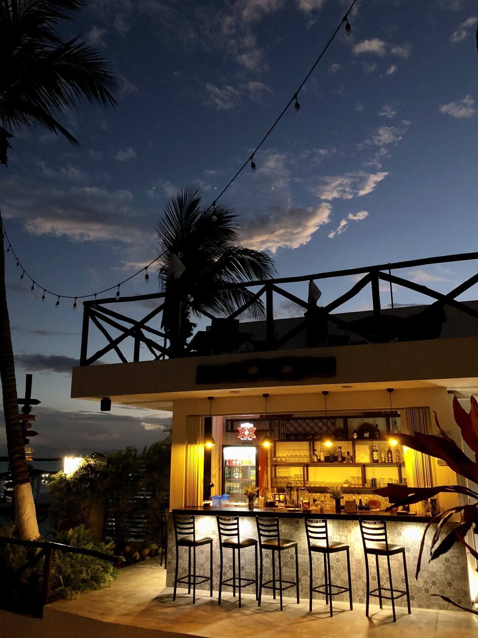 Aldea 19 Bacalar: open-air bar with stools, a palm tree and string lights