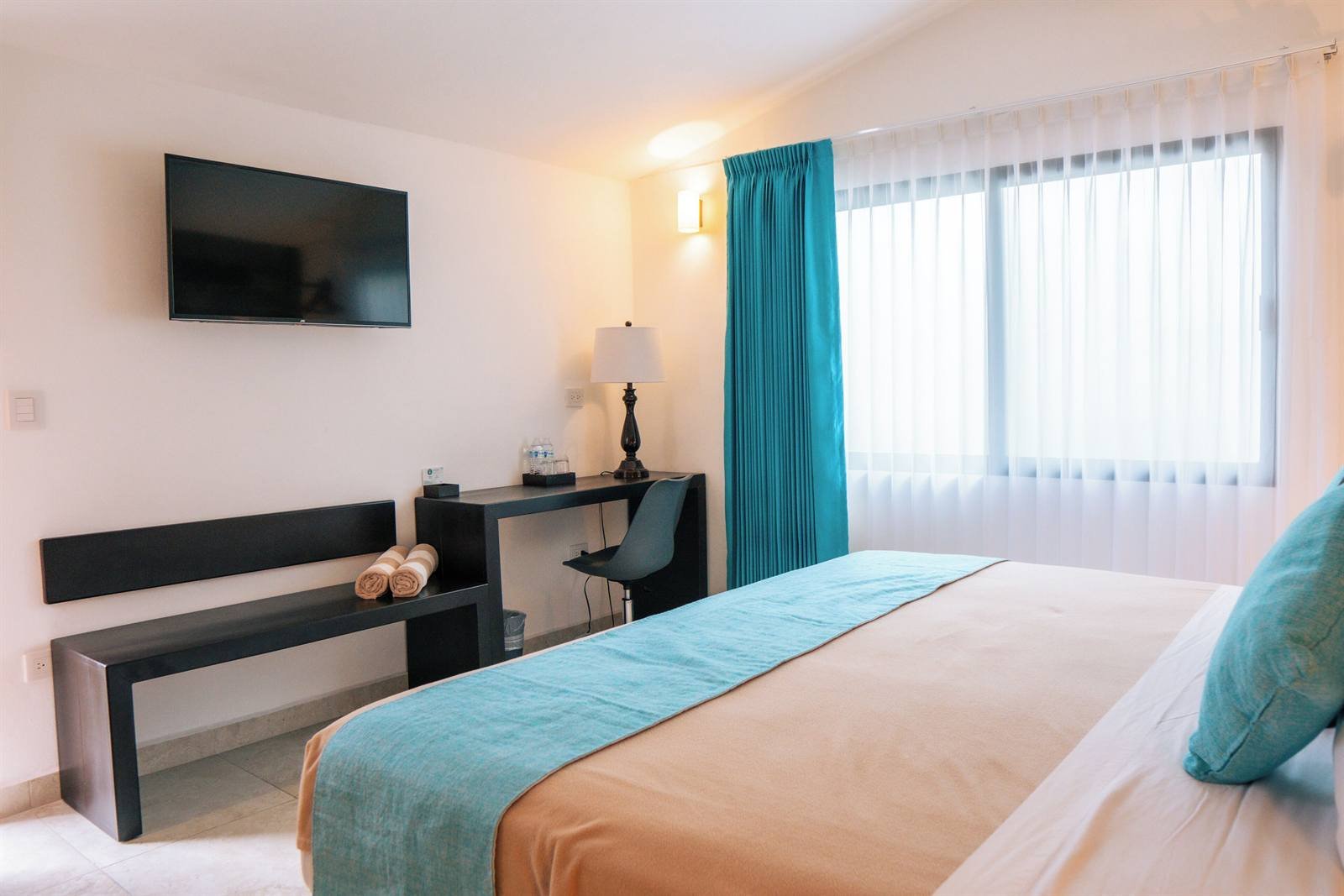Aldea 19 Bacalar: king room with a desk, wall-mounted TV and turquoise curtains